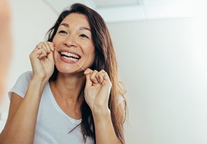 Woman smiling while flossing her teeth in bathroom