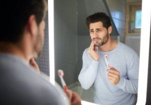 Man with lost dental crown holding cheek in pain