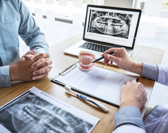 Dentist and patient discussing the four step dental implant tooth replacement process