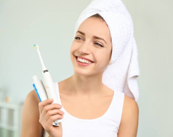 Woman smiling and holding at home dental hygiene products