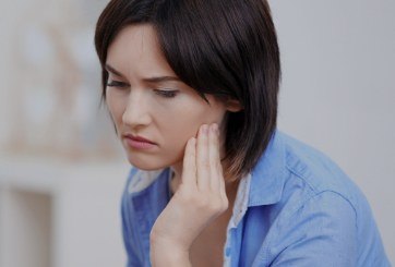 Woman in need of T M J therapy holding jaw in pain