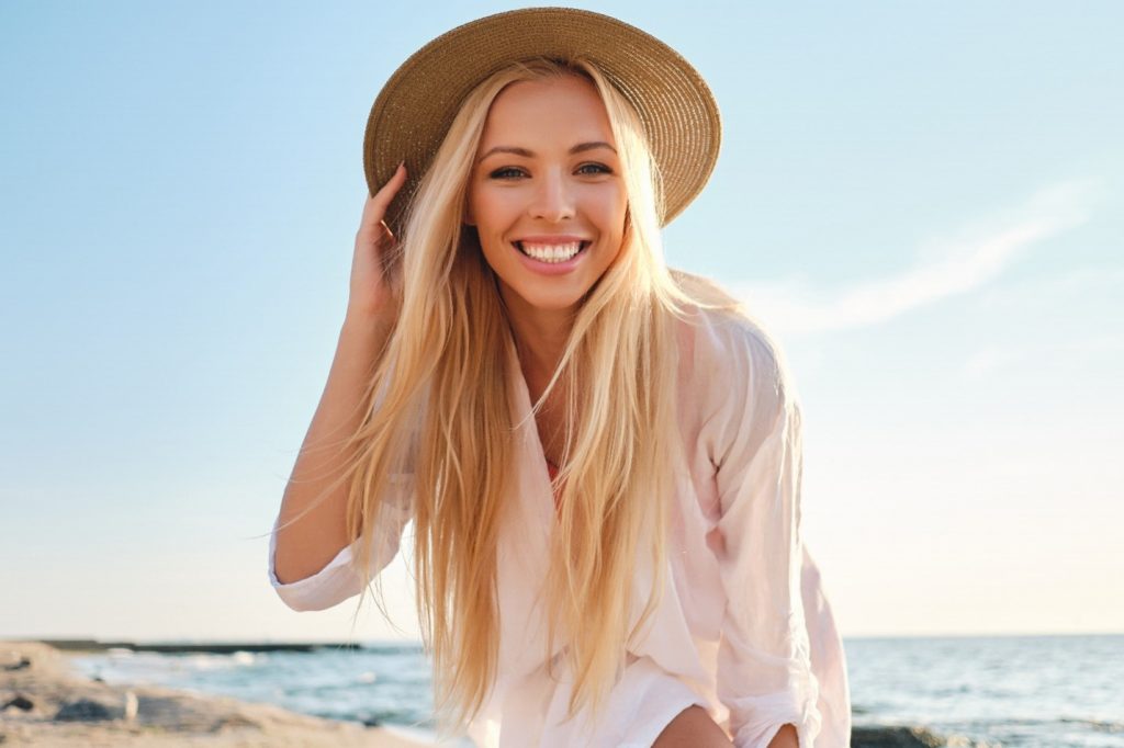 Woman with porcelain veneers smiling at the beach.