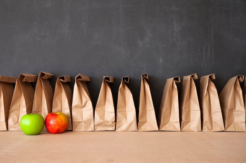 Row of sideways paper bags on a brown counter top against a black wall with one green and one red apple in front of them